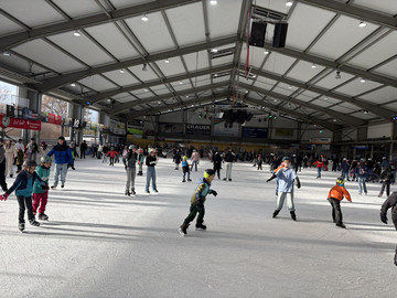 Schlittschuhhalle mit Sonnenschein, viele Kinder fahren Schlittschuh